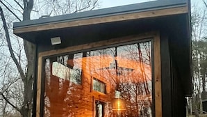 Eine kleine, abgeschlossene Holzhütte mit einem Bett, einem Tisch und einer Hängeleuchte.