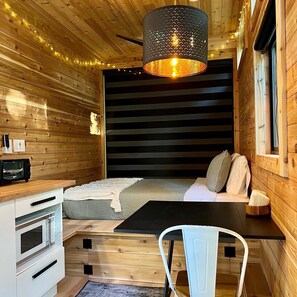 A compact, modern room with a bed, a small kitchenette, and a dining area. - The Dogwood Tiny House (Logan)