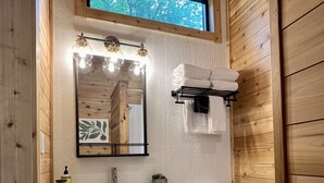 Ein kleines Badezimmer mit Holzvertäfelung, einem weißen Waschbecken, einem spiegeln mit Beleuchtung, einer Toilette und einem Fenster über dem Waschbecken.