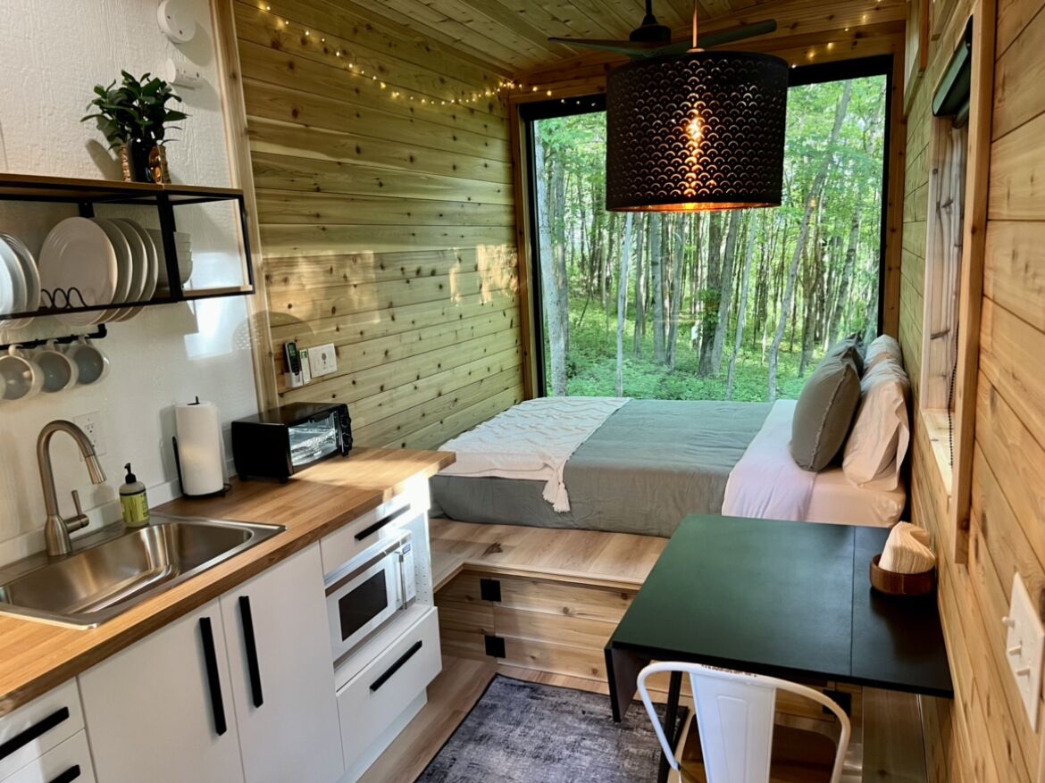 Una cabaña compacta con kitchenette, una cama con vistas al bosque y un comedor.