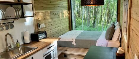 Ein gemütliches Blockhaus mit Küchenzeile, einem Bett mit Blick auf den Wald und einer Essecke.