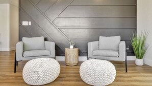 Un salon moderne avec deux canapés gris, une table basse ronde en bois et un pouf blanc en tricot.