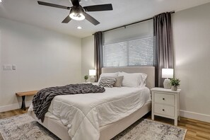 Une chambre à coucher avec un lit, des tables de chevet, un ventilateur de plafond et une fenêtre avec des rideaux.