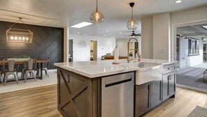 Une cuisine moderne dotée d’un îlot central, de luminaires suspendus et d’un coin repas agrémenté d’un motif géométrique sur un mur.