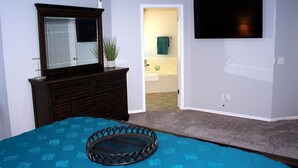 A bedroom with a bed, a dresser, a TV, and a bathroom visible through an open door. - Modern and stylish 3 bedroom with large layout floor plan (Lawton)