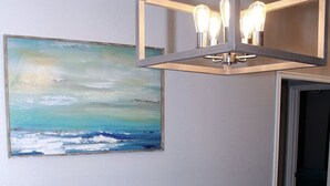 A dining area with a wooden table and chairs, a pendant light fixture, and a painting of a seascape on the wall. - Modern and stylish 3 bedroom with large layout floor plan (Lawton)