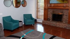 A living room with teal armchairs, a fireplace, and a TV on the wall. - Modern and stylish 3 bedroom with large layout floor plan (Lawton)