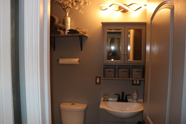 A bathroom with a toilet, sink, mirror, and shelves with toiletries.