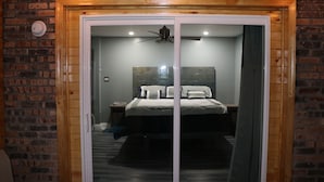 A bedroom with a bed, a nightstand, a ceiling fan, and a brick wall.