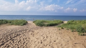 A sandy beach with footprints leading to the water, under a partly cloudy sky.