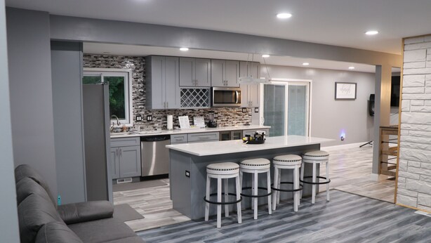 A modern kitchen with grey cabinets, a central island with stools, a microwave, and a dishwasher.