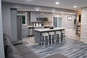 A modern kitchen with grey cabinets, a central island with stools, a microwave, and a dishwasher.