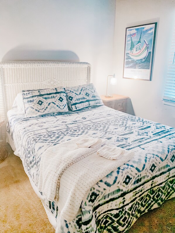 A bed with a white and blue patterned bedspread, a white woven headboard, and a framed picture on the wall.