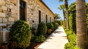 A stone building with a long, straight pathway flanked by lush greenery and palm trees. -  Voger Alaçatı Social (Cesme)