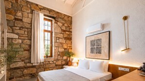 Une chambre avec un mur en pierre, un lit, une fenêtre avec des rideaux, une table de chevet, une lampe et un luminaire suspendu.