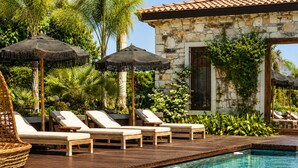 Un espace aménagé au bord de la piscine, avec des chaises longues, des parasols et un bâtiment en pierre.