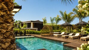 A swimming pool with lounge chairs and umbrellas, surrounded by greenery and a modern building. -  Voger Alaçatı Social (Cesme)