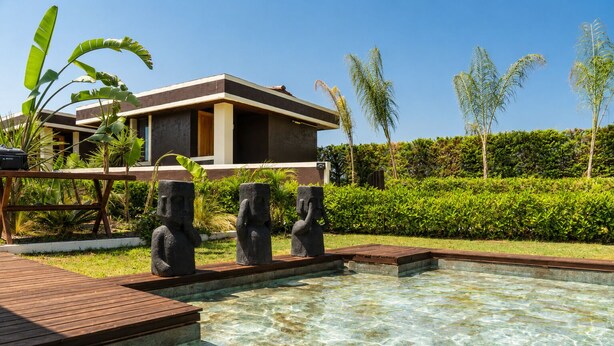 A swimming pool with clear water, surrounded by a wooden deck and three stone statues. -  Voger Alaçatı Social (Cesme)