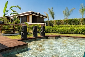 A swimming pool with clear water, surrounded by a wooden deck and three stone statues. -  Voger Alaçatı Social (Cesme)