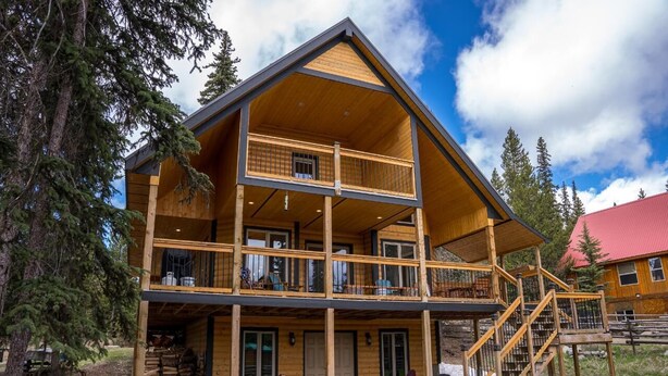 A two-story log cabin with a balcony and a staircase leading to the upper floor. - Stewart Family Cabin by Face Lake (Logan Lake)