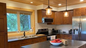 A modern kitchen with wooden cabinets, a large island, stainless steel appliances, and pendant lighting. - Stewart Family Cabin by Face Lake (Logan Lake)