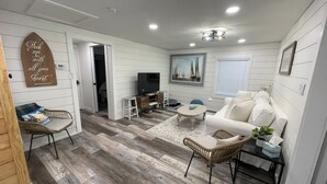 A modern living room with a white sofa, a television, and a wooden floor.