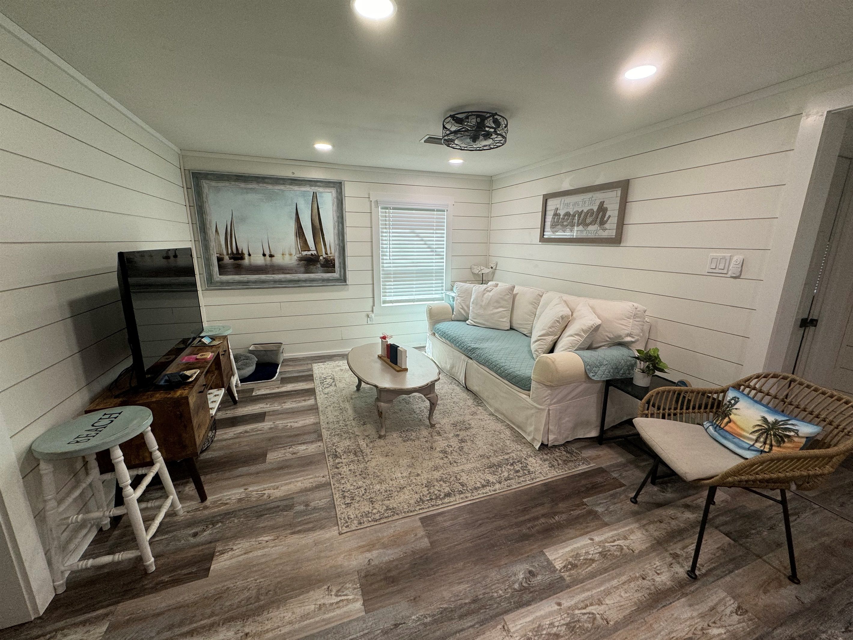 A compact living space with a sofa, a small table, a wicker chair, a television, and a painting on the wall.