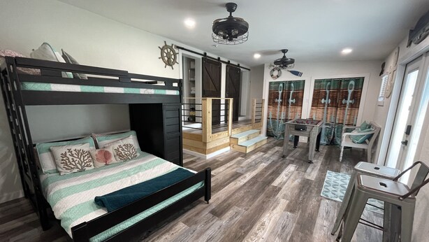 A bunk bed with a desk and chair, a foosball table, and a window with curtains.