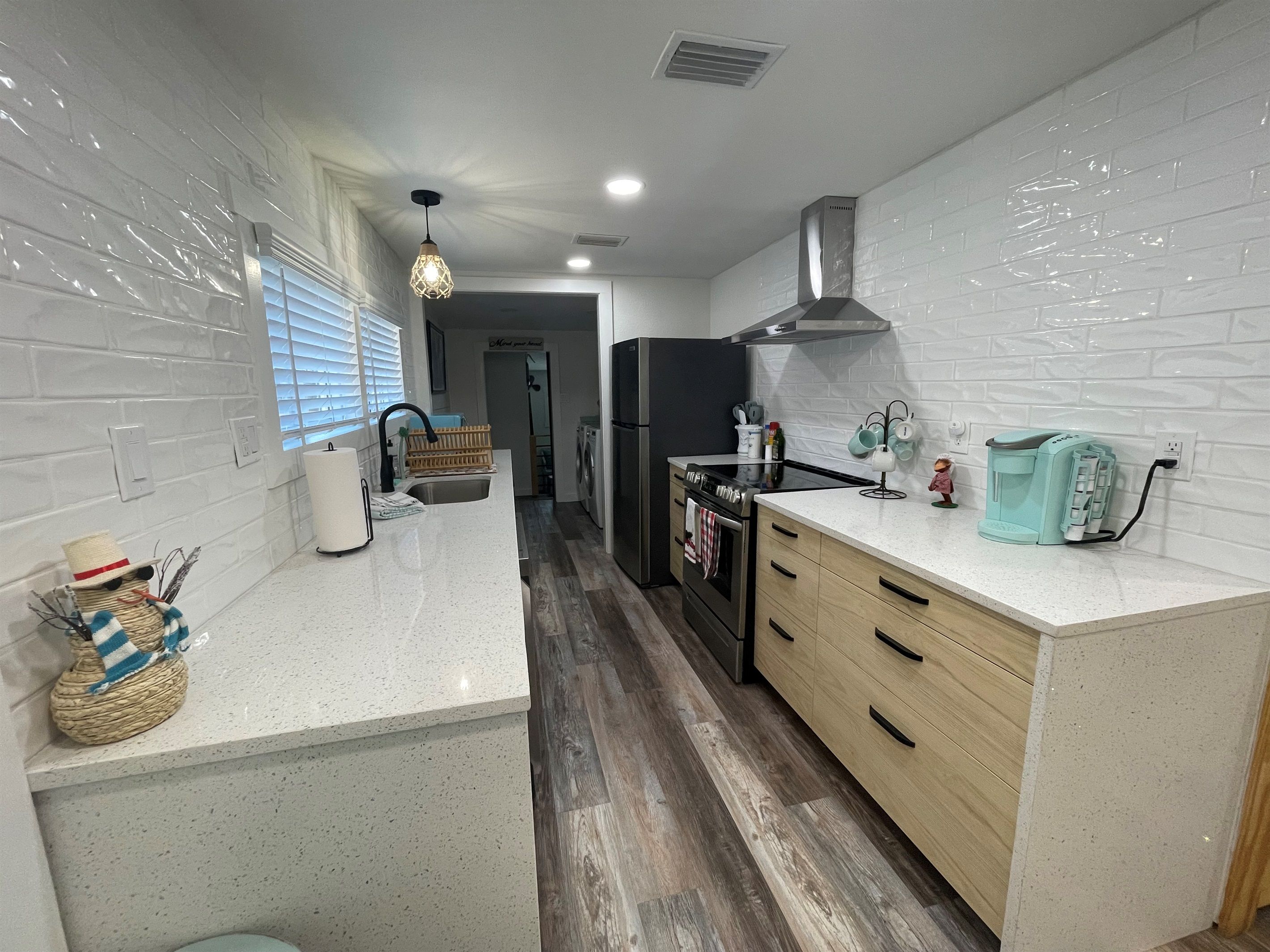 Una cocina moderna con azulejos blancos tipo metro, piso de madera, estufa de acero inoxidable y una cafetera color turquesa.