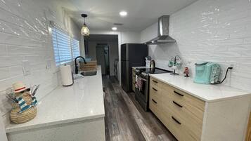 Una cocina moderna con azulejos blancos tipo metro, piso de madera, estufa de acero inoxidable y una cafetera color turquesa.