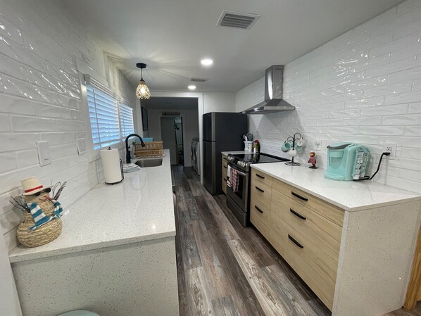 A modern kitchen with white subway tiles, wooden flooring, a stainless steel range, and a teal coffee machine.