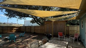Une terrasse extérieure avec une table et des chaises en bois, un espace ombragé et une cour clôturée.