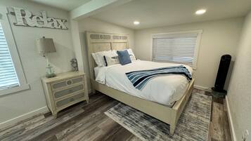 A bedroom with a bed, nightstand, lamp, and a wall sign.