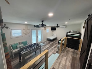 A compact living space with a foosball table, a bed, a desk, and a ceiling fan.