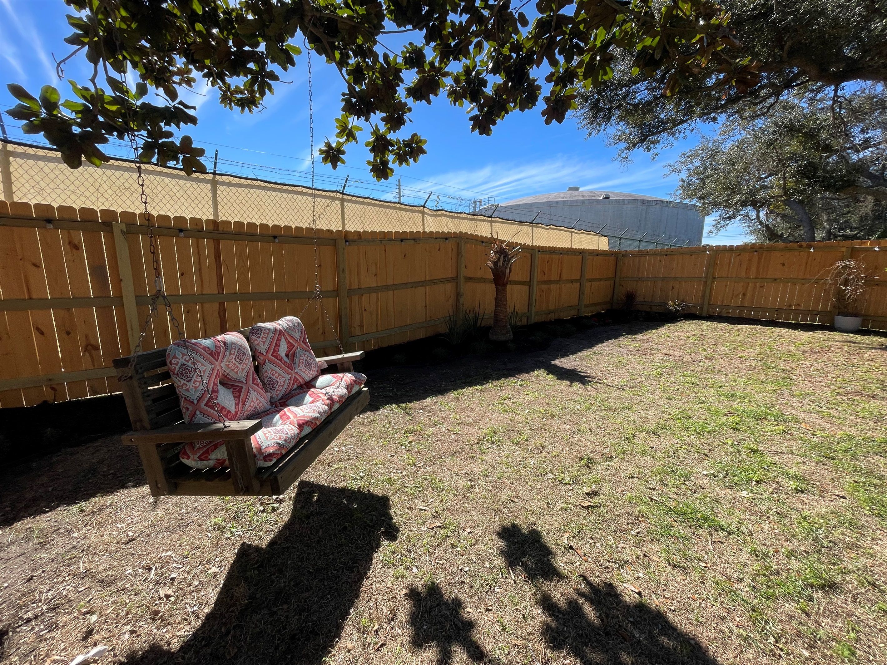 Un jardin avec une clôture en bois, un banc en bois agrémenté de coussins à motifs et un petit palmier.