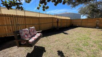 Un jardin avec une clôture en bois, un banc en bois agrémenté de coussins à motifs et un petit palmier.