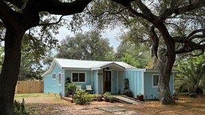 Une maison de plain-pied avec un porche, entourée d’arbres et d’une clôture en bois.