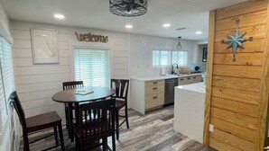 A modern kitchen with a dining area, wooden flooring, and a welcome sign.