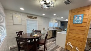 Une cuisine moderne avec un îlot central en bois, un coin repas avec une table ronde et des chaises, et un panneau « Bienvenue » accroché au mur.
