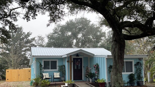 Une petite maison avec un porche à l’avant, une boîte aux lettres et une clôture en bois en arrière-plan.