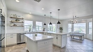 A spacious kitchen with white cabinetry, a large island, and a view of the outdoors through large windows. - Beautiful Hemet Home: Large Patio & Mtn Views! (Hemet)