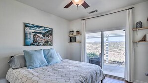 A bedroom with a bed, a ceiling fan, a window with a view of the desert, and a painting on the wall. - Beautiful Hemet Home: Large Patio & Mtn Views! (Hemet)
