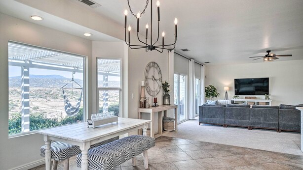 A spacious living area with a large window, a dining table with benches, a sofa, and a television. - Beautiful Hemet Home: Large Patio & Mtn Views! (Hemet)