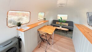 A compact RV interior with a kitchenette, a dining table, a sofa, and two windows.
