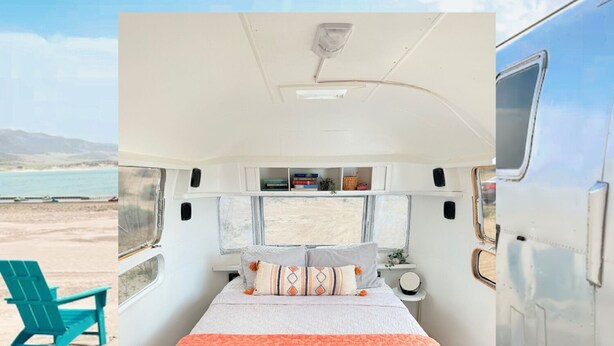 A cozy RV bedroom with a bed, pillows, and a window overlooking a beach.