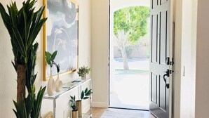 A hallway with a large painting, a console table with decorative items, a potted plant, and a door leading outside. - Great location,Best value, beautiful home+games (Indio)