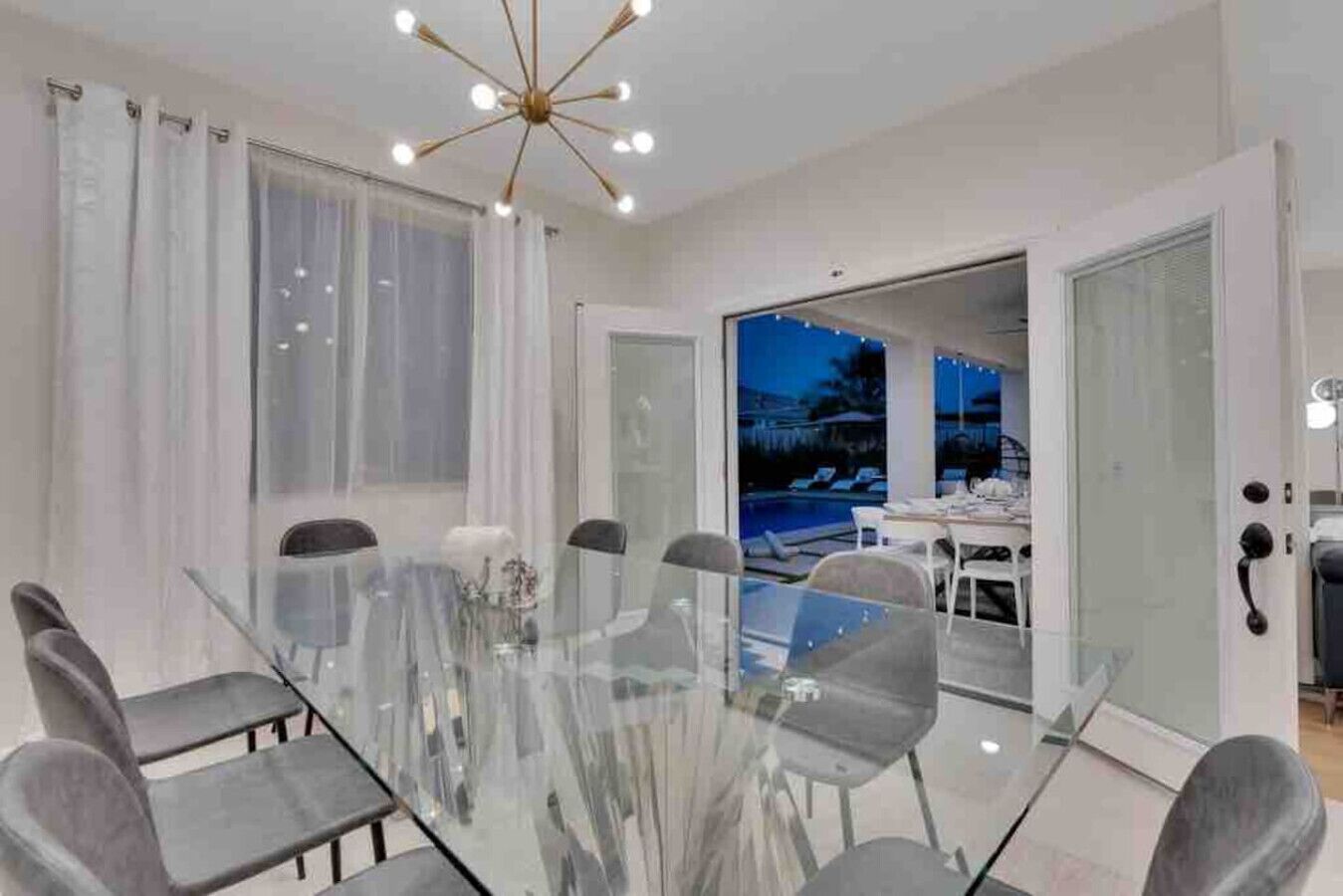 Comedor moderno con una mesa y sillas de vidrio, un candelabro y vistas a una zona de piscina.