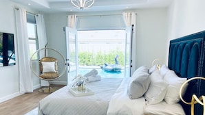 A modern bedroom with a large bed, a circular hanging chair, and a view of a swimming pool. - Great location,Best value, beautiful home+games (Indio)