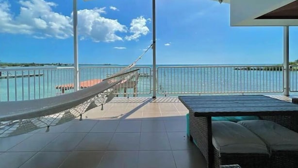 Un espacio al aire libre techado con una hamaca, un sofá de mimbre y vista al mar.