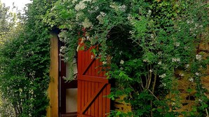 A building partially covered with green ivy, a red gate, and a yellow door. - Pretty country house with large garden (Diges)